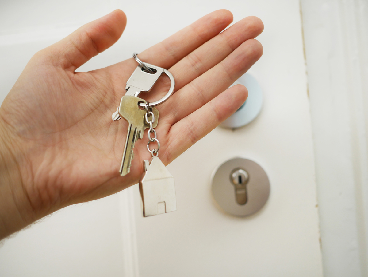 adult hand holding house keys in front of a door